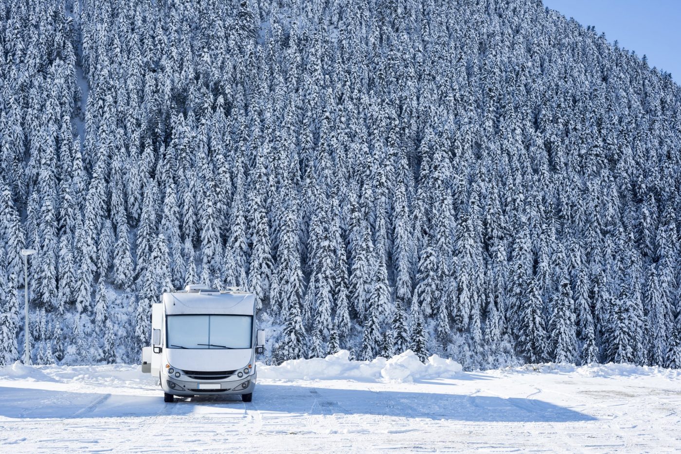 Wohnmobil campt im Schnee vor Nadelwald