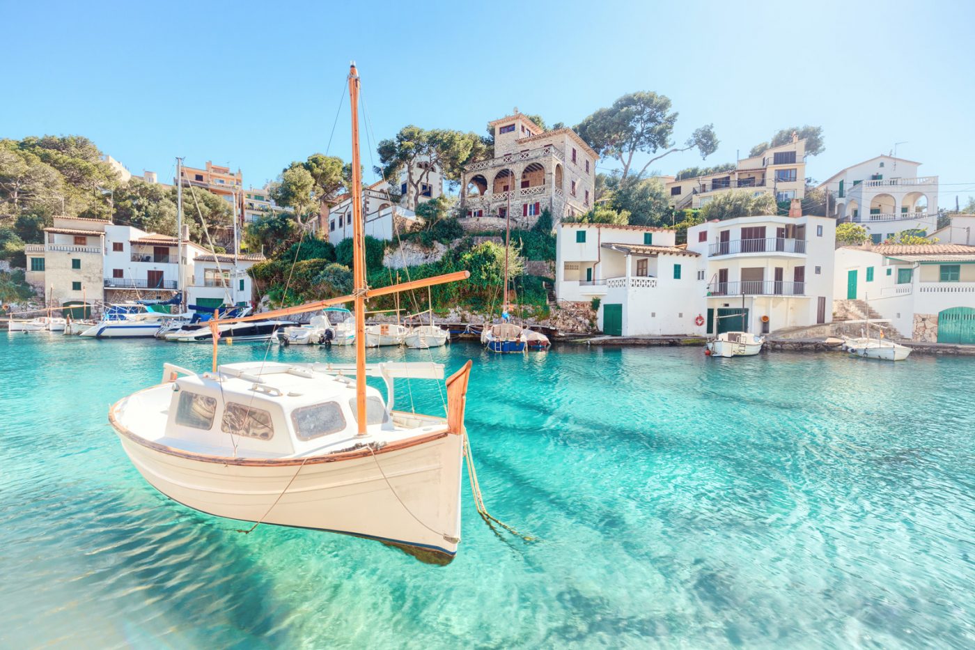 Ein Segelboot auf blauem Wasser vor weißen Häusern an der Küste von Mallorca.