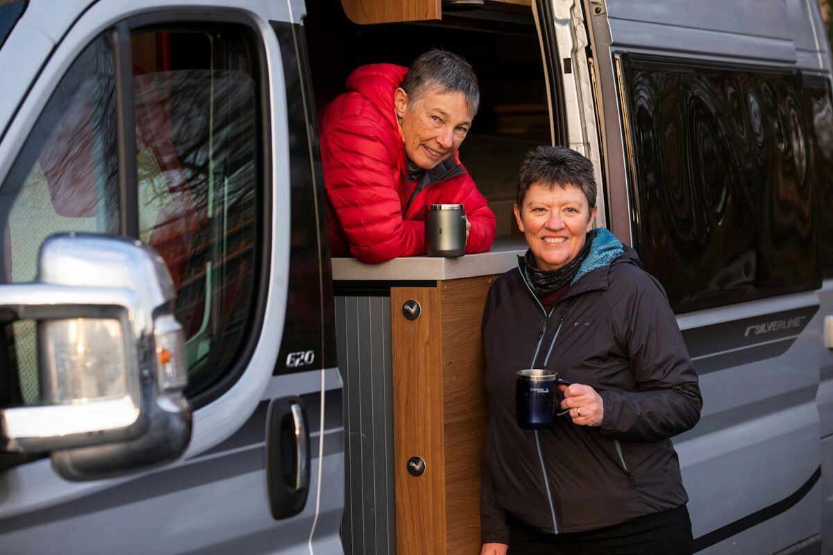 Zwei Damen trinken Kaffee an einem Campervan